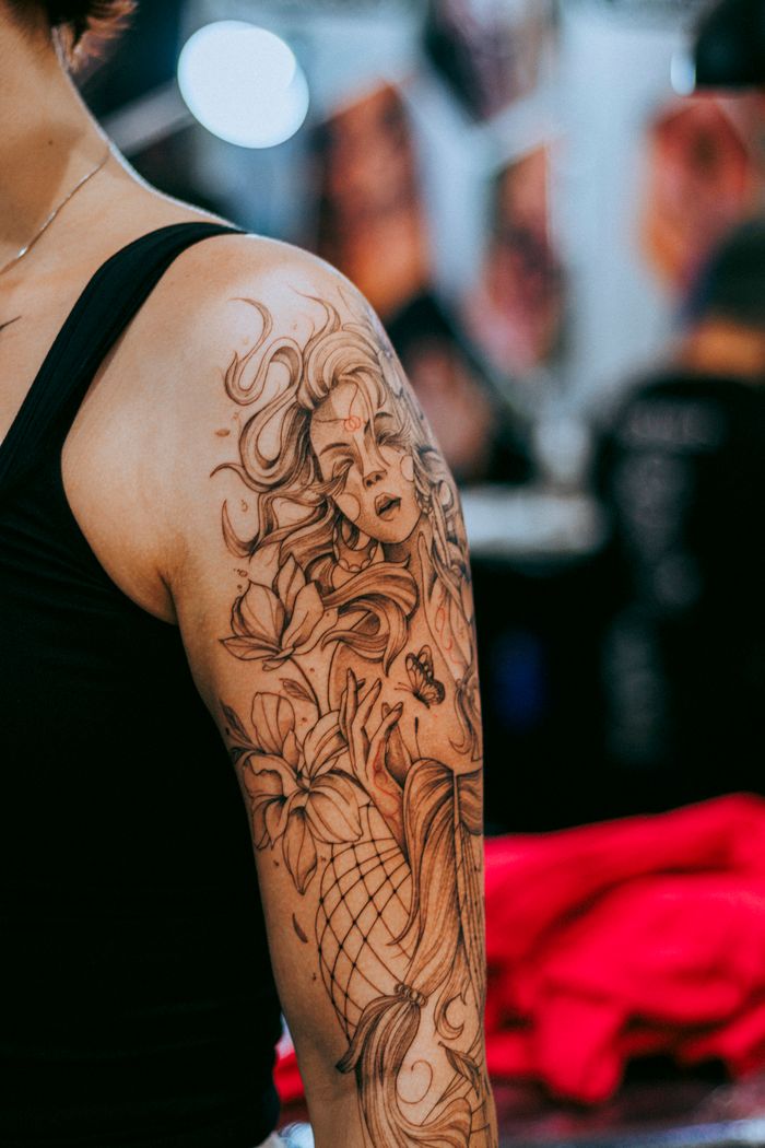 gallery-2 Detailed arm tattoo featuring floral and mythical elements on a woman's shoulder.