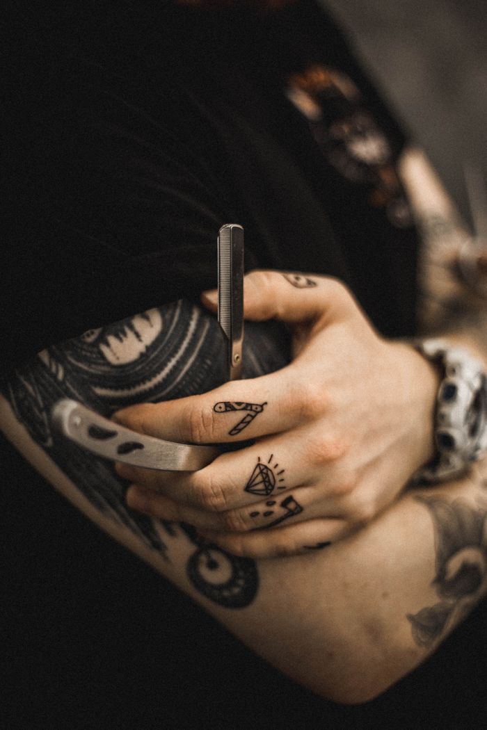 why-choose-us Close-up of a tattooed arm holding a straight razor, showcasing intricate designs.